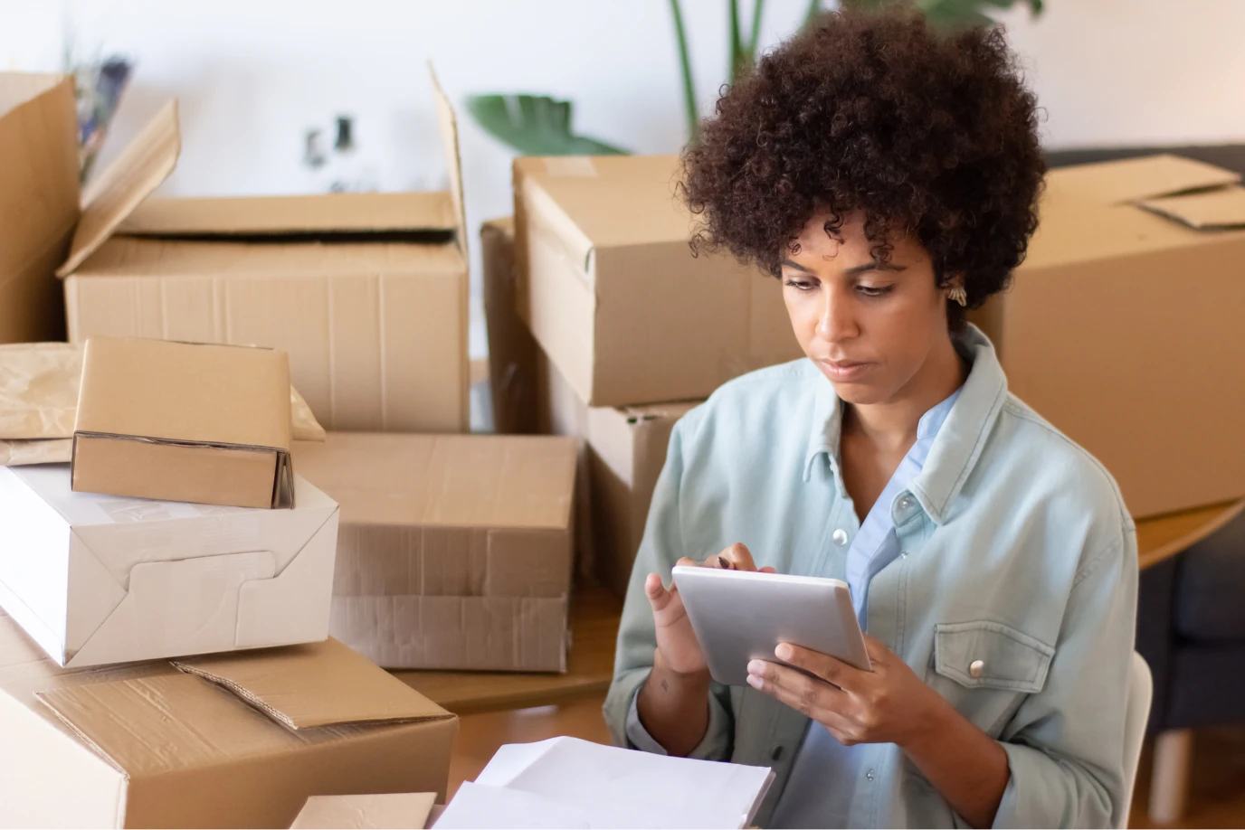 Small business owner checking orders on a tablet among packed shipping boxes.